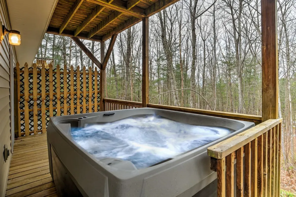 A well-appointed outdoor area featuring a hot tub on a wooden deck, framed by surrounding trees for privacy. The scene evokes restfulness and the enjoyment of nature right at home.