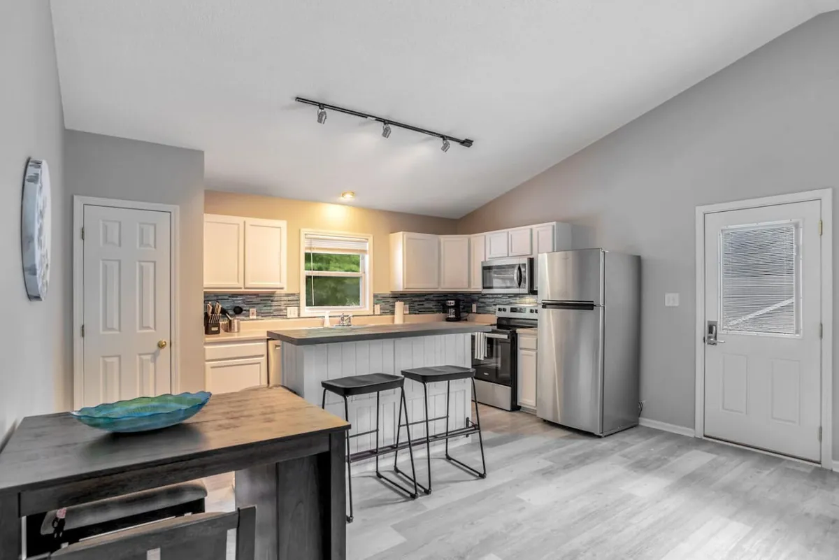 A modern kitchen featuring a large island with bar stools, stainless steel appliances, and a window that lets in abundant natural light. The cheerful mood is complemented by stylish fixtures and a practical layout designed for easy meal preparation and group gatherings.