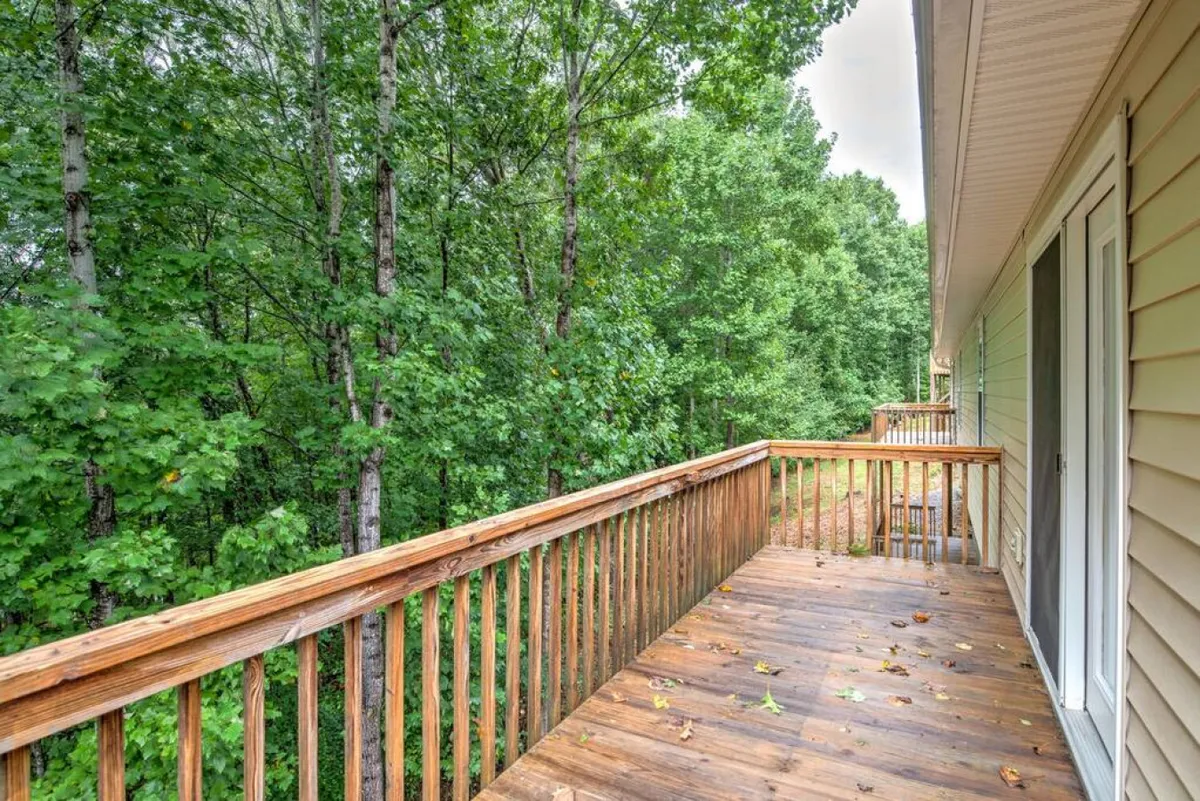 A serene exterior image focusing on a wooden deck set among tall, leafy trees. The area looks peaceful and inviting, perfect for morning coffee, evening chats, or simply enjoying the fresh mountain air with a pet by your side.