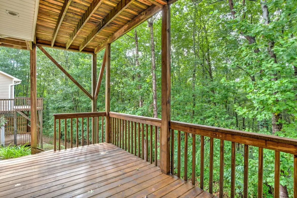 A peaceful exterior shot of a spacious wooden deck bordered by lush greenery. The scene suggests a private, serene outdoor space ideal for relaxing, entertaining, or spending time with pets. The deck is open and inviting, with views of nature and room for outdoor furniture or gatherings.