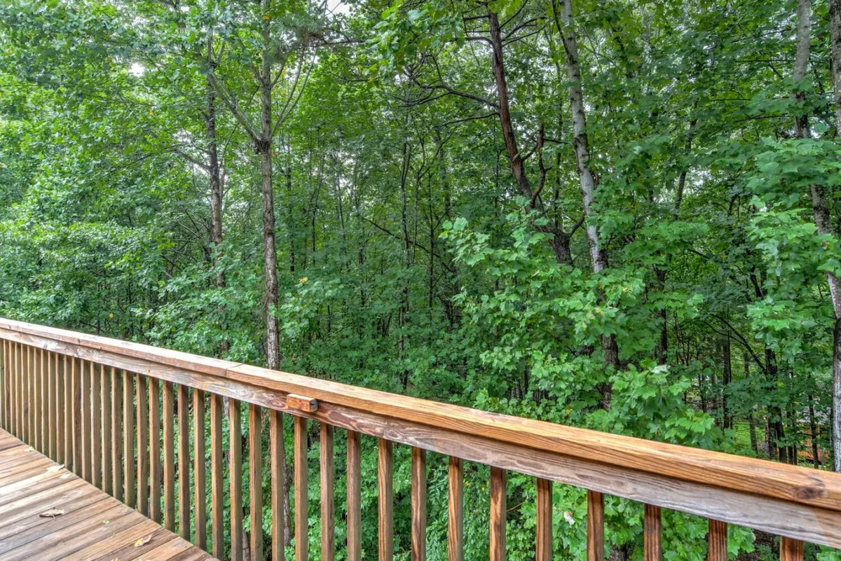An inviting exterior view featuring a wooden railing overlooking dense greenery. The deck provides a tranquil setting for relaxing outdoors, with nature views all around, and hints at the peacefulness of the neighborhood.