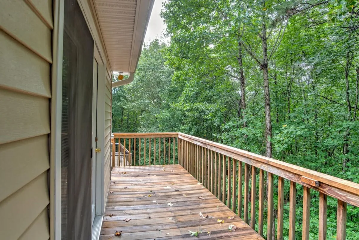 A wooden deck attached to the home, bordered by vibrant green foliage. The scene suggests space for outdoor relaxation or casual family gatherings, blending the home into the natural environment.